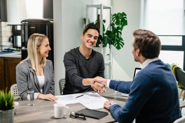 Happy couple shaking hands with their real estate agent at home. Insurance and Loan